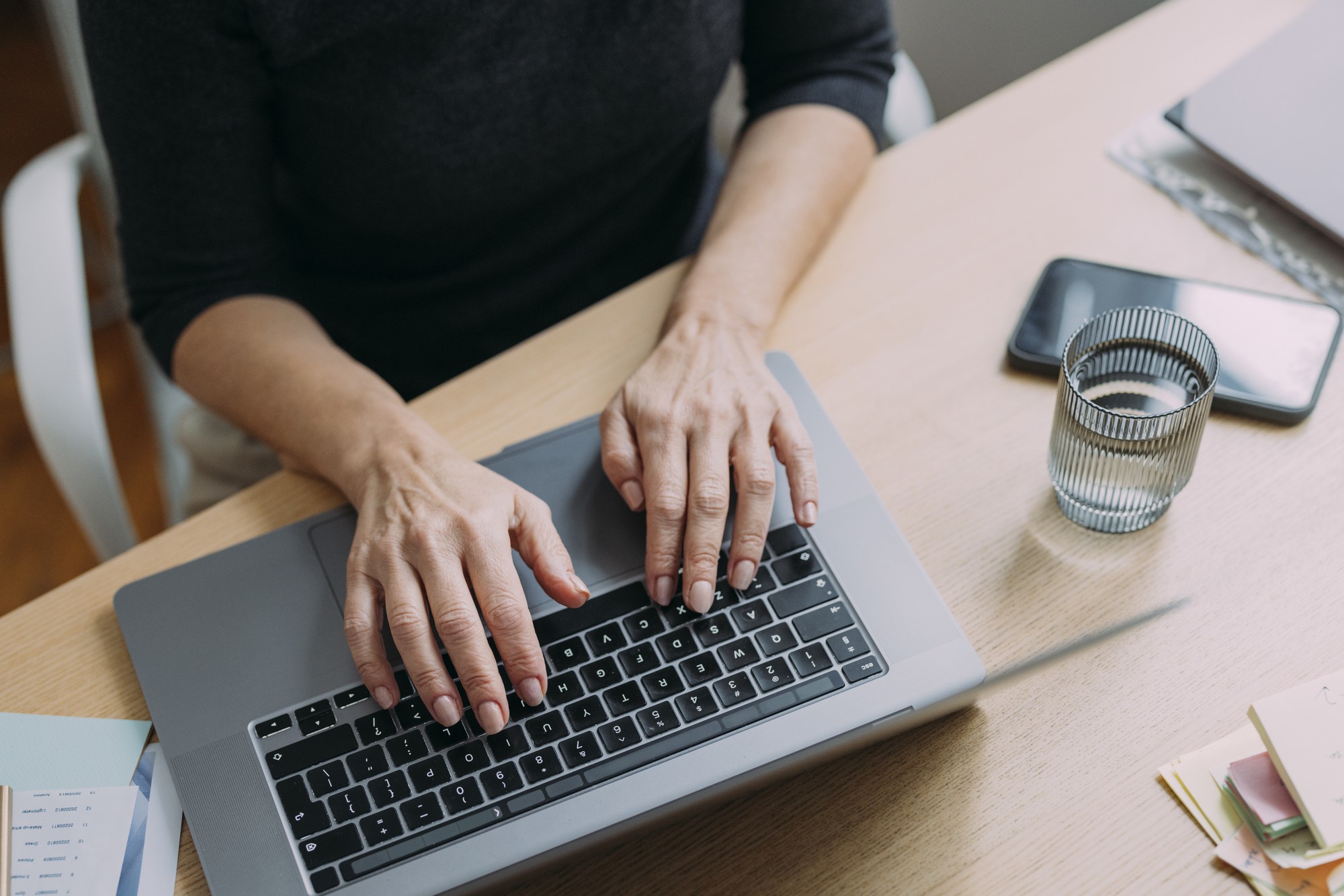 Person sitzt am Schreibtisch und schreibt auf Laptop-Tastatur